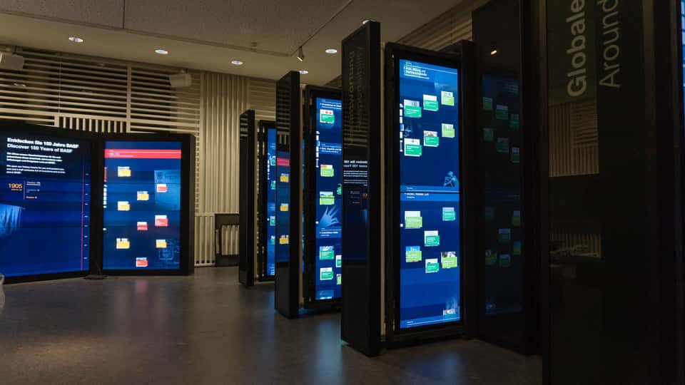 Angled view through multiple rows of vertical touchscreen panels in the BASF History Library, highlighting the depth, modular layout, and spatial organization of the interactive exhibition system.