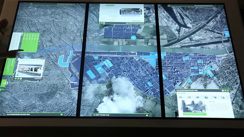 Multi-user interaction on a large-format multitouch table showing layered site data, imagery, and informational panels.