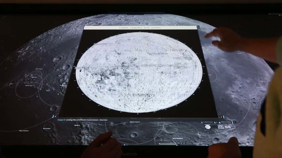 Photo of the Moontable installation with a big popup window showing additional information about a specific lunar feature, while users interact with the multi-touch table.