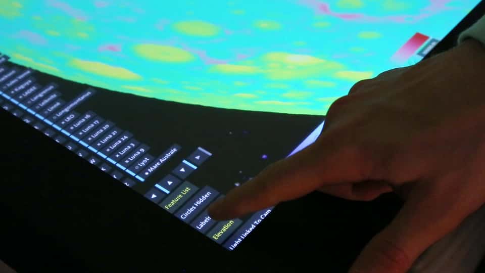 A close-up photo of the Moontable's interactive surface, showing detailed lunar features and a finger interacting with the touch-enabled table.